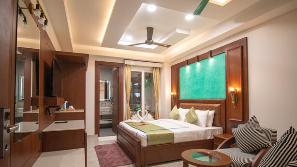 A hotel room with a bed, a seating area with a round table, a vanity with a mirror, and a ceiling fan. - Holy Shivana Boutique Hotel Rishikesh (Narendranagar)