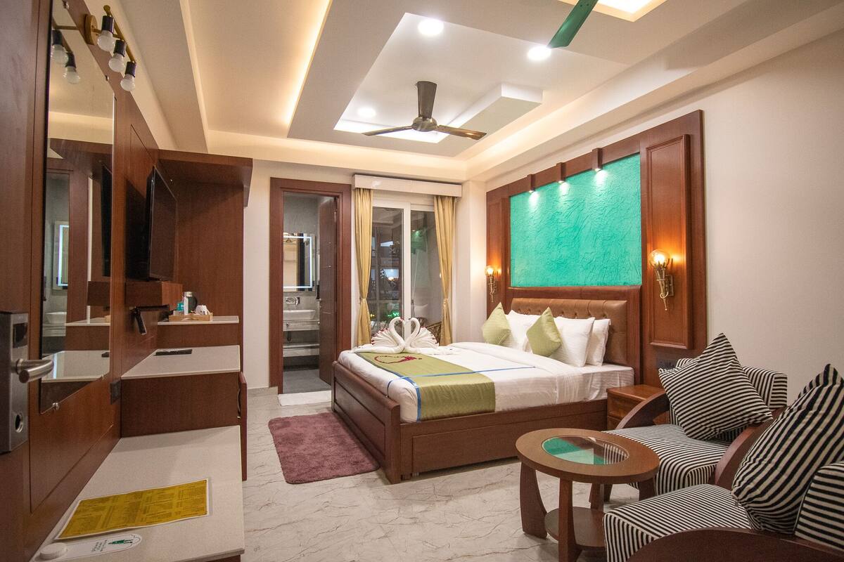 A hotel room with a bed, a seating area with a round table, a vanity with a mirror, and a ceiling fan.