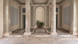 Een klassieke architectonische gang met zuilen, een middendeur en een potplant.