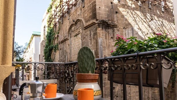 Een tafel met een koffiezetapparaat en oranje bekers op een balkon met een sierijzeren hekwerk en een gebouw op de achtergrond.