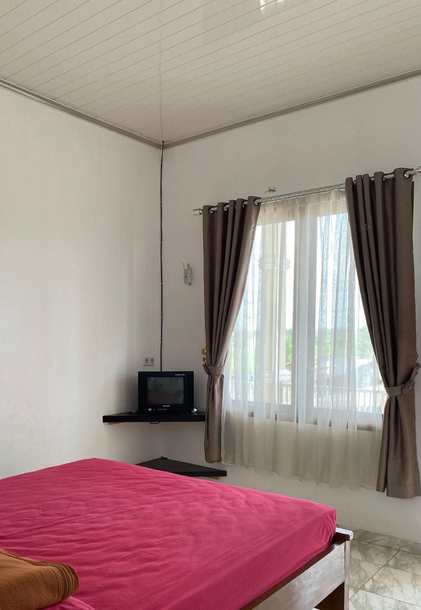A room with a bed, a television on a stand, and a window with curtains.