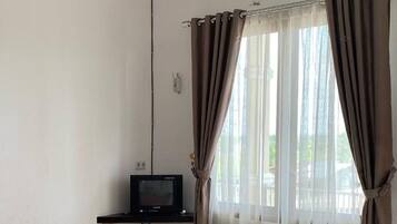 A room with a bed, a television on a stand, and a window with curtains.
