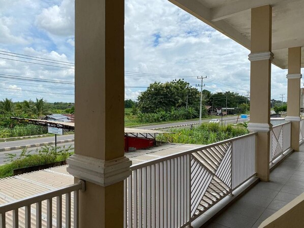 A balcony with a view of a road, greenery, and a cloudy sky.