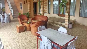 A covered outdoor seating area with wicker furniture, a table, and potted plants.