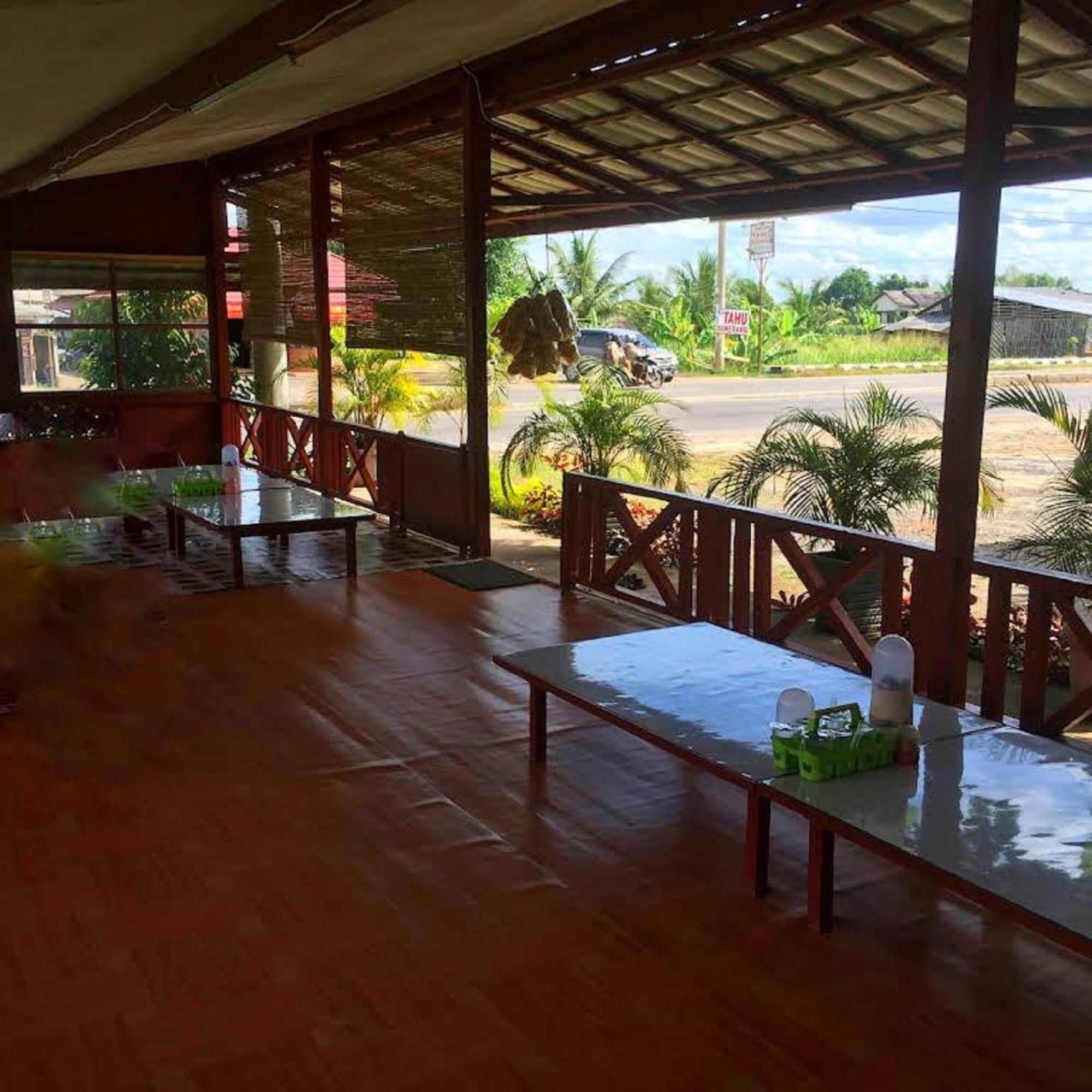 An indoor area with wooden flooring and tables, a covered outdoor section with a view of the street and greenery.