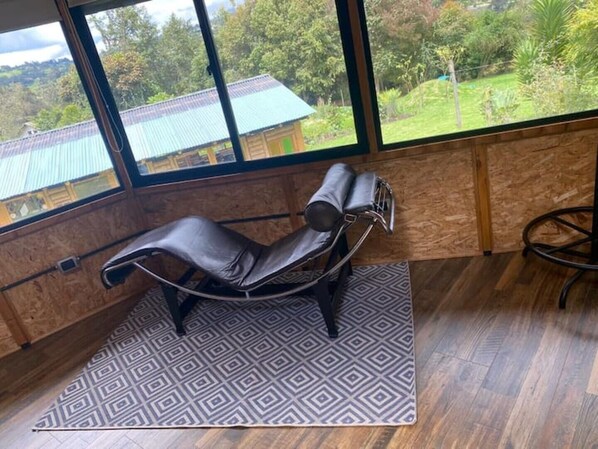 A room with a massage chair, large windows with a view of a house and greenery, and a patterned rug. - Magical yurt with a hot tub in Tabio (Tabio)