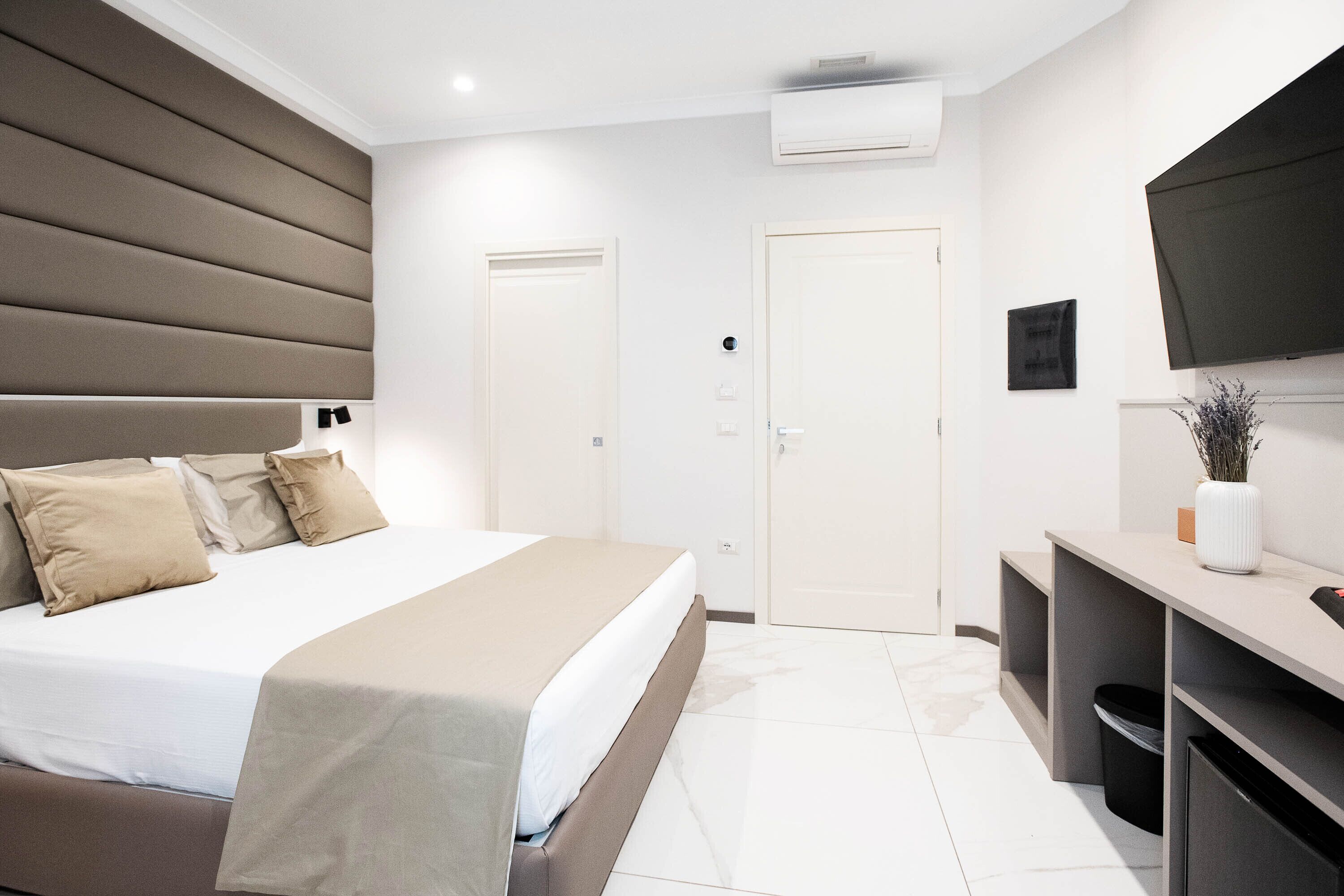 Una camera d'hotel moderna con un letto grande, una televisione a schermo piatto, una scrivania e un cestino.