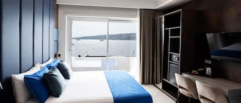 Quarto de hotel moderno com uma cama grande, uma mesa de escritório, uma televisão e vista para a água.