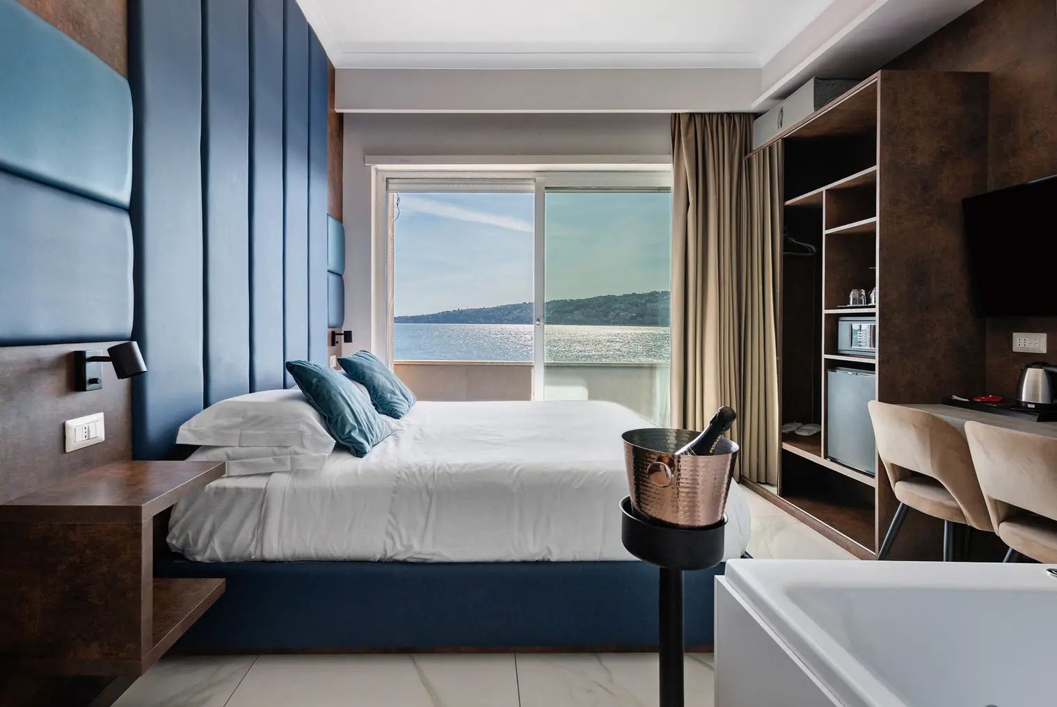 Habitación de hotel con cama, un minibar, televisión y vista al mar.