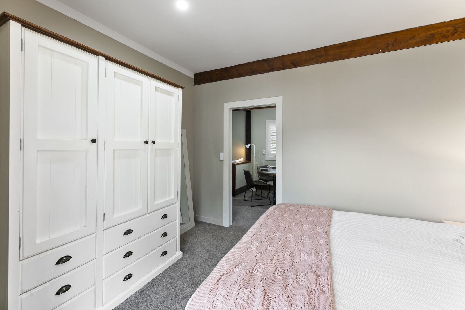 Een slaapkamer met een grote kledingkast, een bed met een roze deken en een bureau met een stoel.