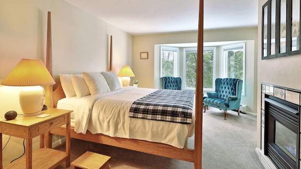 A bedroom with a four-poster bed, bedside lamps, a blue armchair, and a fireplace. - The Birch Ridge: Blue Velvet Room #10 - Queen Suite in Killington, Vermont. Hot Tub. Lounge. (Killington)
