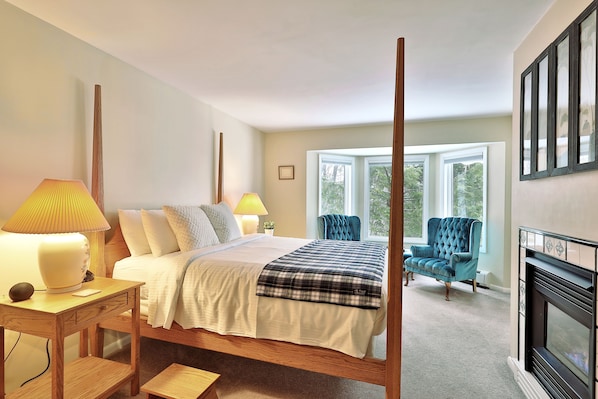A bedroom with a four-poster bed, bedside lamps, a blue armchair, and a fireplace. - The Birch Ridge: Blue Velvet Room #10 - Queen Suite in Killington, Vermont. Hot Tub. Lounge. (Killington)