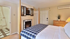 A bedroom with a bed, a fireplace, a television mounted above it, a door, and a dresser. - The Birch Ridge: Blue Velvet Room #10 - Queen Suite in Killington, Vermont. Hot Tub. Lounge. (Killington)