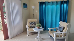 A room with two white armchairs, a small round table with a potted plant, and a blue curtain.