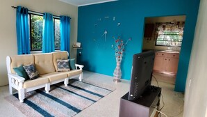 A living room with a beige sofa, a television, and a kitchen area visible through an open door.