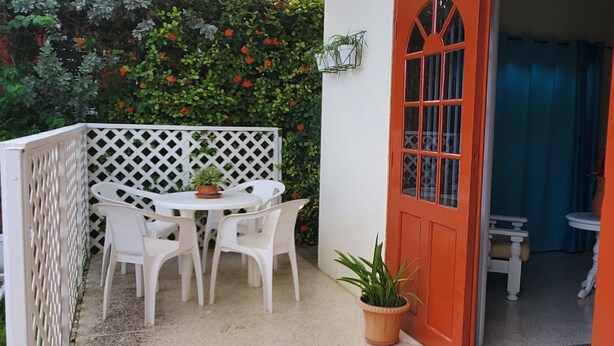 A patio with a white table and chairs, a potted plant, and a red door.