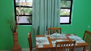 A dining table set with plates, glasses, and cutlery, positioned in front of a window with a view of greenery.