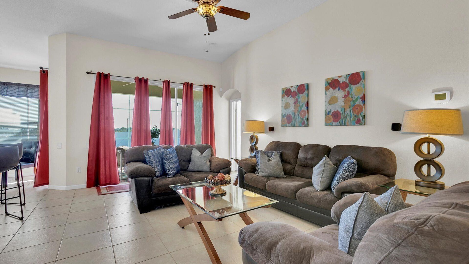 A spacious living room with two sofas, a glass coffee table, and a ceiling fan.