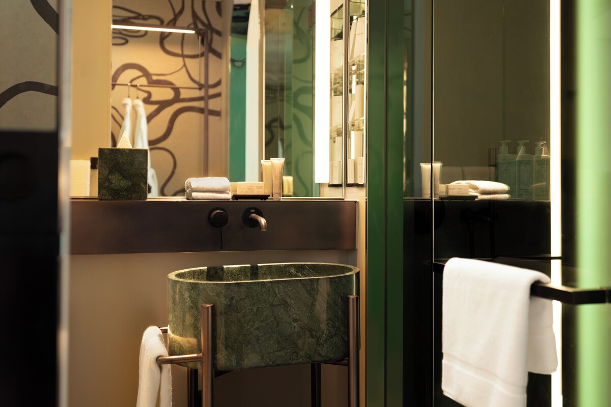 A bathroom with a marble sink, a towel rack, and a mirror reflecting toiletries.