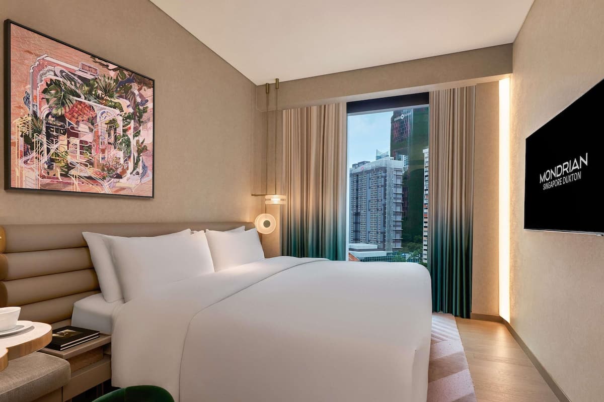 Een hotelkamer met een bed, een bureau, een stoel, een schilderij en uitzicht op een gebouw.
