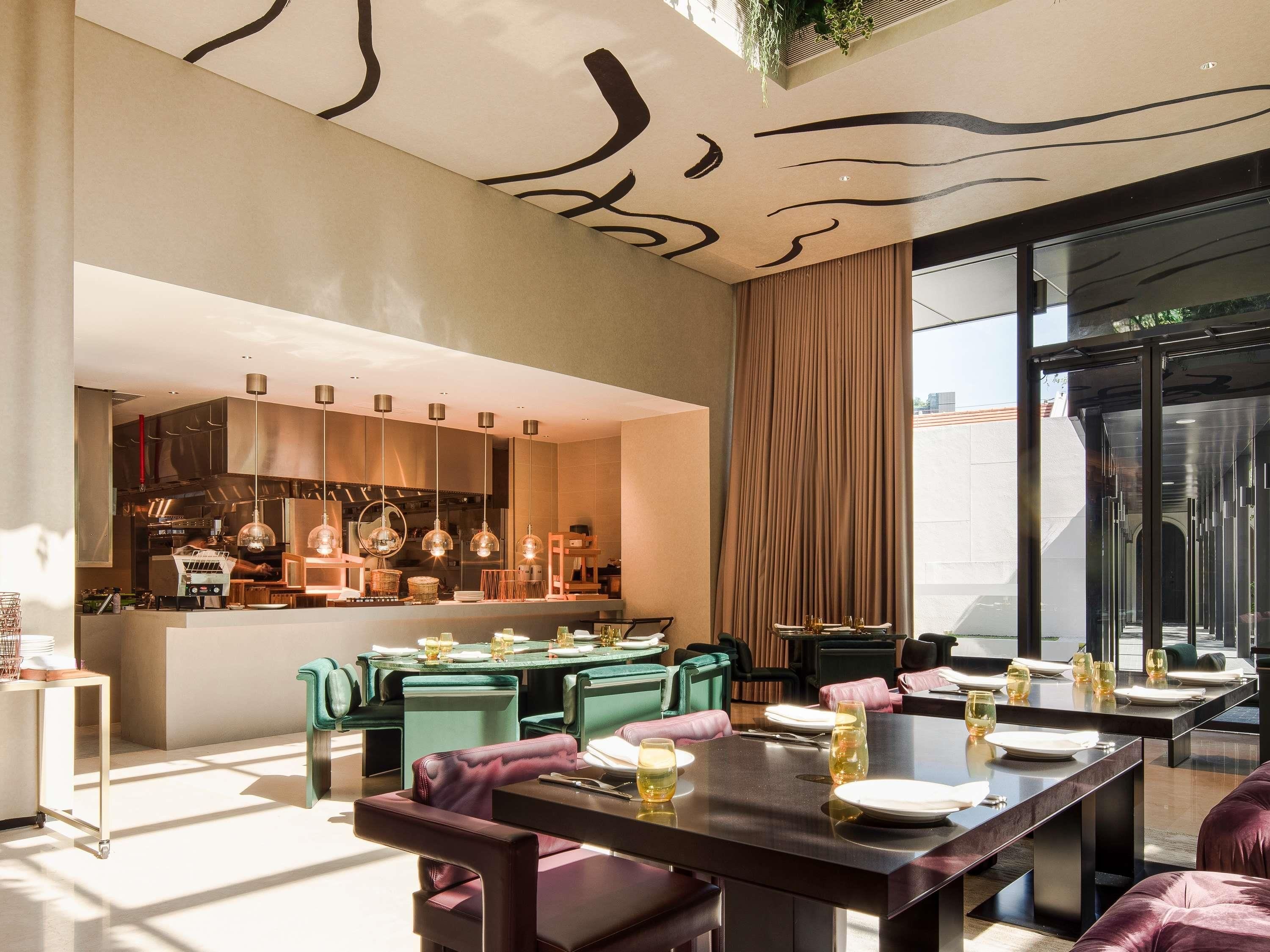 A modern dining area with a central bar, green upholstered chairs, and a large window with a view.