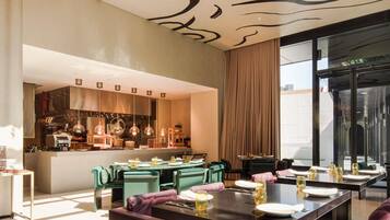 A modern dining area with a central bar, green upholstered chairs, and a large window with a view.