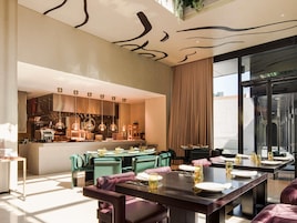 A modern dining area with a central bar, green upholstered chairs, and a large window with a view.