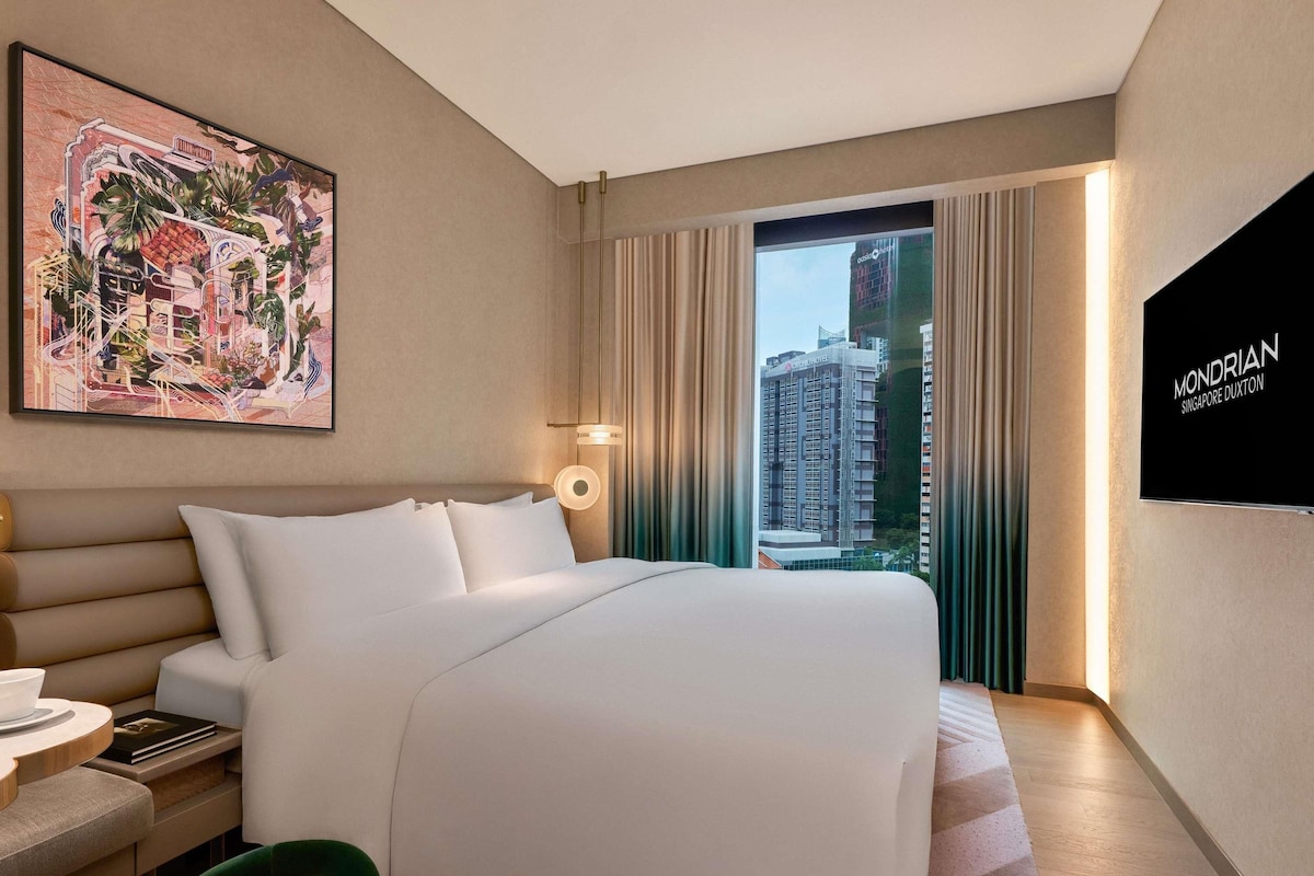 Habitación de hotel con cama, escritorio, silla, un cuadro y vistas a un edificio.