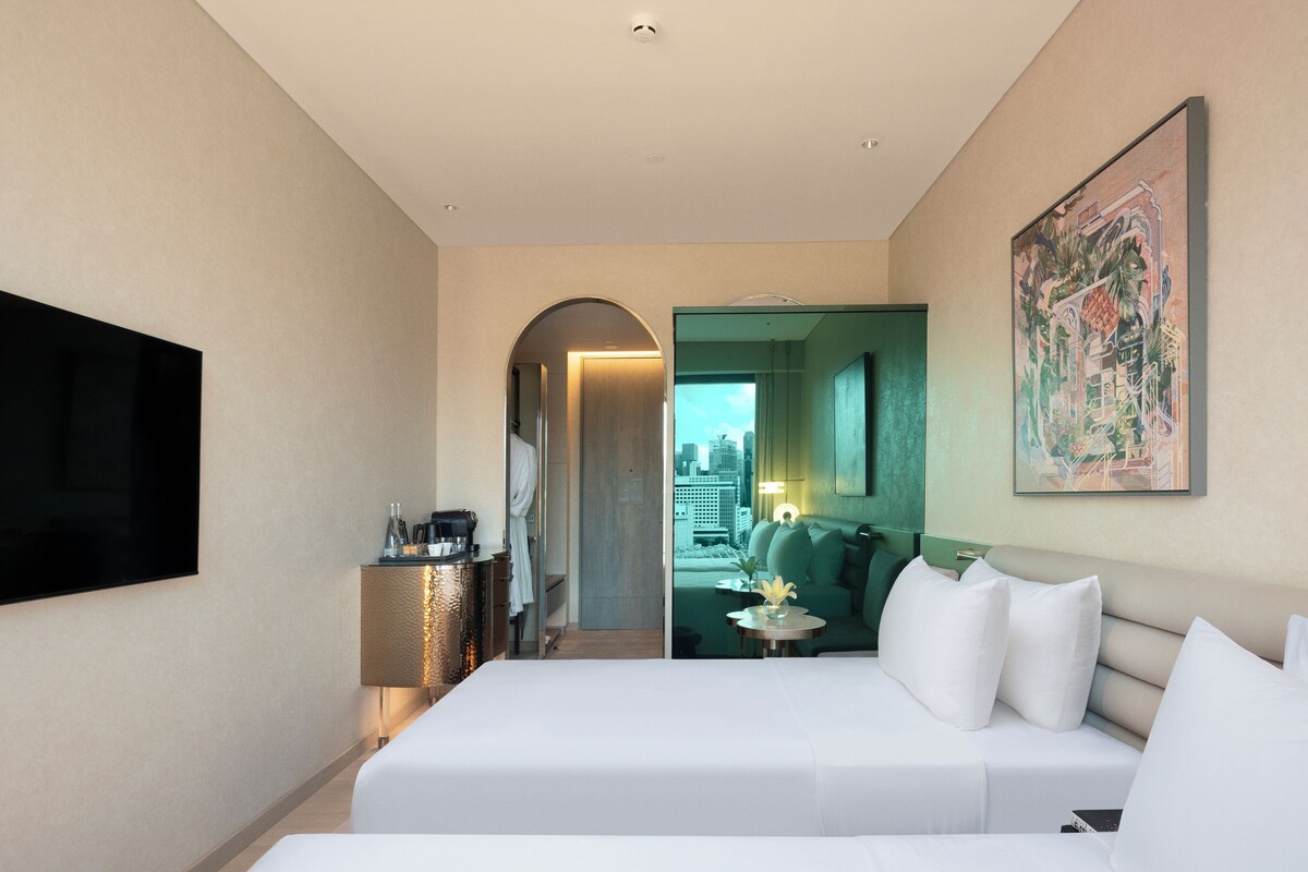 A hotel room with two beds, a TV, a minibar, and a city view.