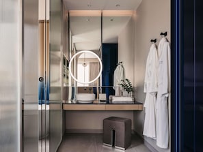 Een moderne badkamer met een grote spiegel, een ronde lamp, een wastafel en twee witte badjassen aan haken.