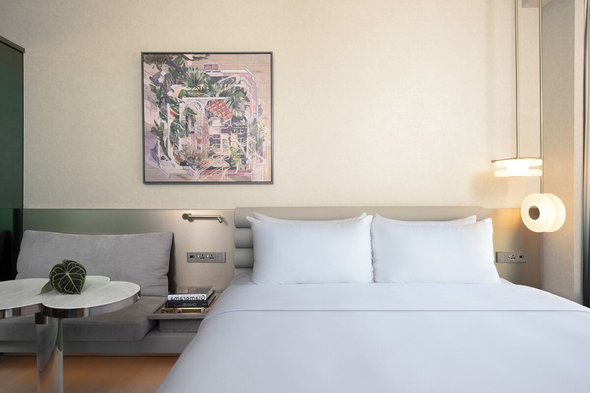 A hotel room with a bed, bedside table, and a wall-mounted artwork.