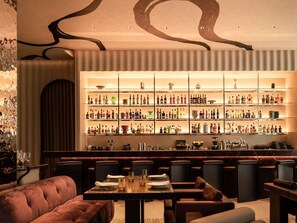 Una zona de bar con varias estanterías llenas de botellas, un espacio de descanso con sillones cómodos y una encimera de mármol.