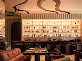 Eine Bar mit mehreren Flaschenregalen, einer Sitzgruppe mit gepolsterten Stühlen und einer Marmorarbeitsplatte.