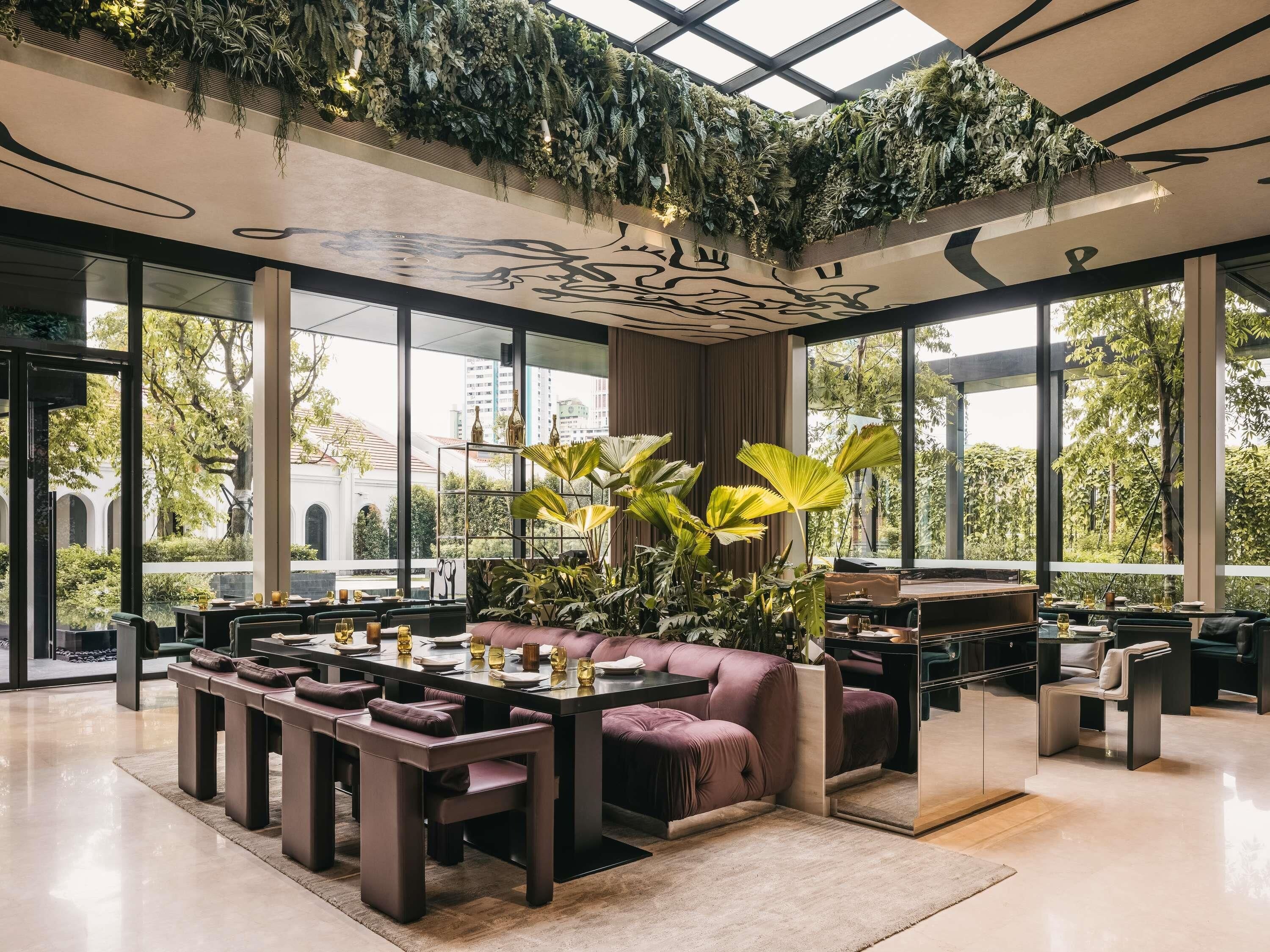 Un espacio interior moderno con comedor, asientos y grandes ventanales que ofrecen vistas al exterior.