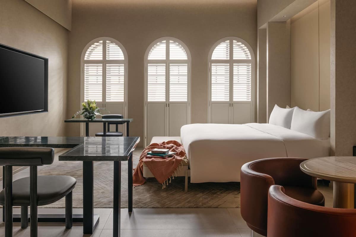 Een moderne hotelkamer met een bed, een flatscreen televisie, een bureau en boogvensters.