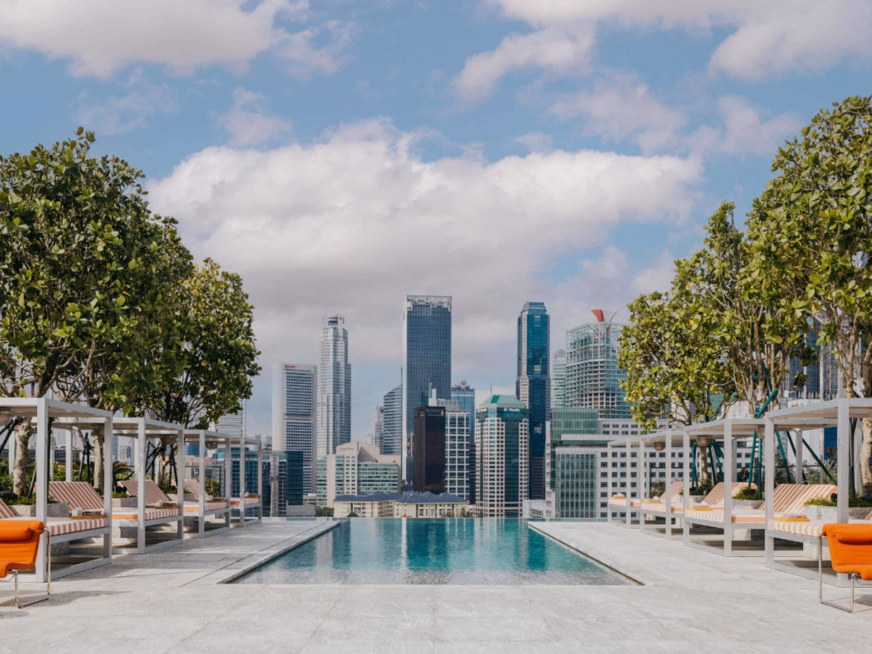 Una piscina en la azotea con sillones de descanso y un horizonte urbano de fondo.