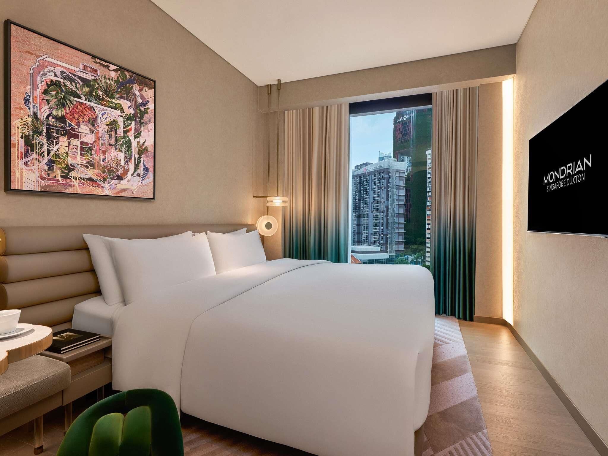 Een hotelkamer met een bed, een bureau met stoel, een schilderij aan de muur en uitzicht op een gebouw.