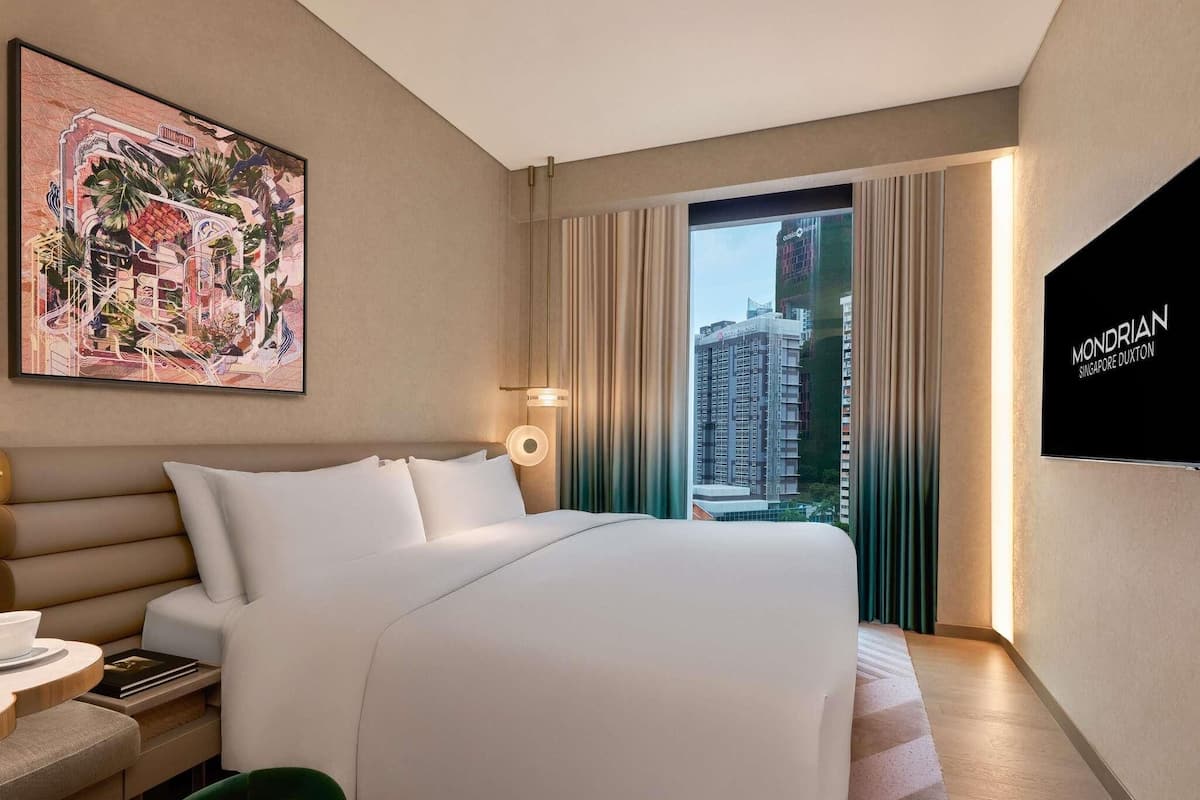 Een hotelkamer met een bed, een bureau met stoel, een schilderij aan de muur en uitzicht op een gebouw.