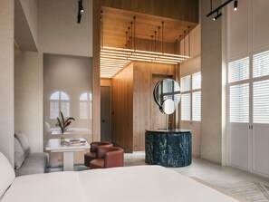 A modern bedroom with a large bed, a round mirror, a small table with books, and a seating area. - Mondrian Singapore Duxton (Singapore)