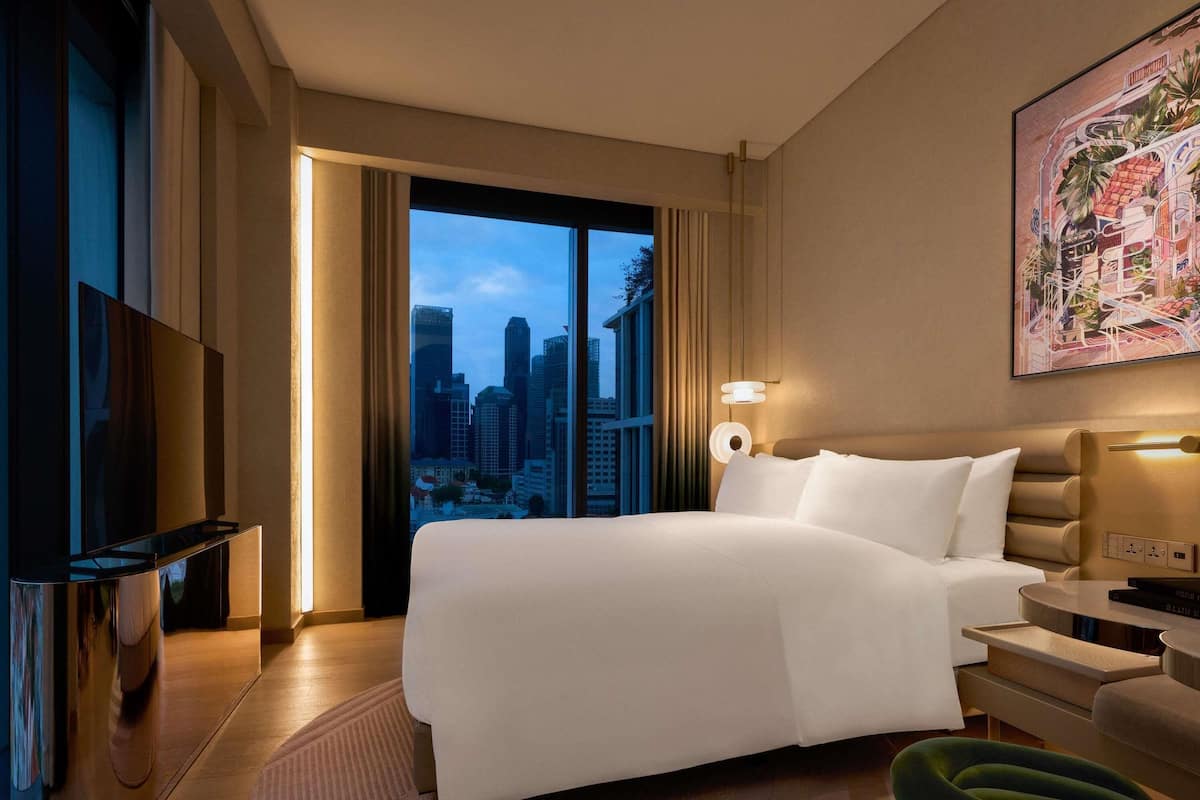 Hotelkamer met een bed, een televisie, een bureau, een stoel en uitzicht over de stad.