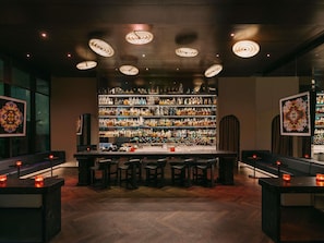 Een bar met een houten visgraatvloer, een bargedeelte met krukken en planken vol flessen.