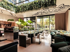 A modern restaurant with indoor plants, round tables, and comfortable seating. - Mondrian Singapore Duxton (Singapore)