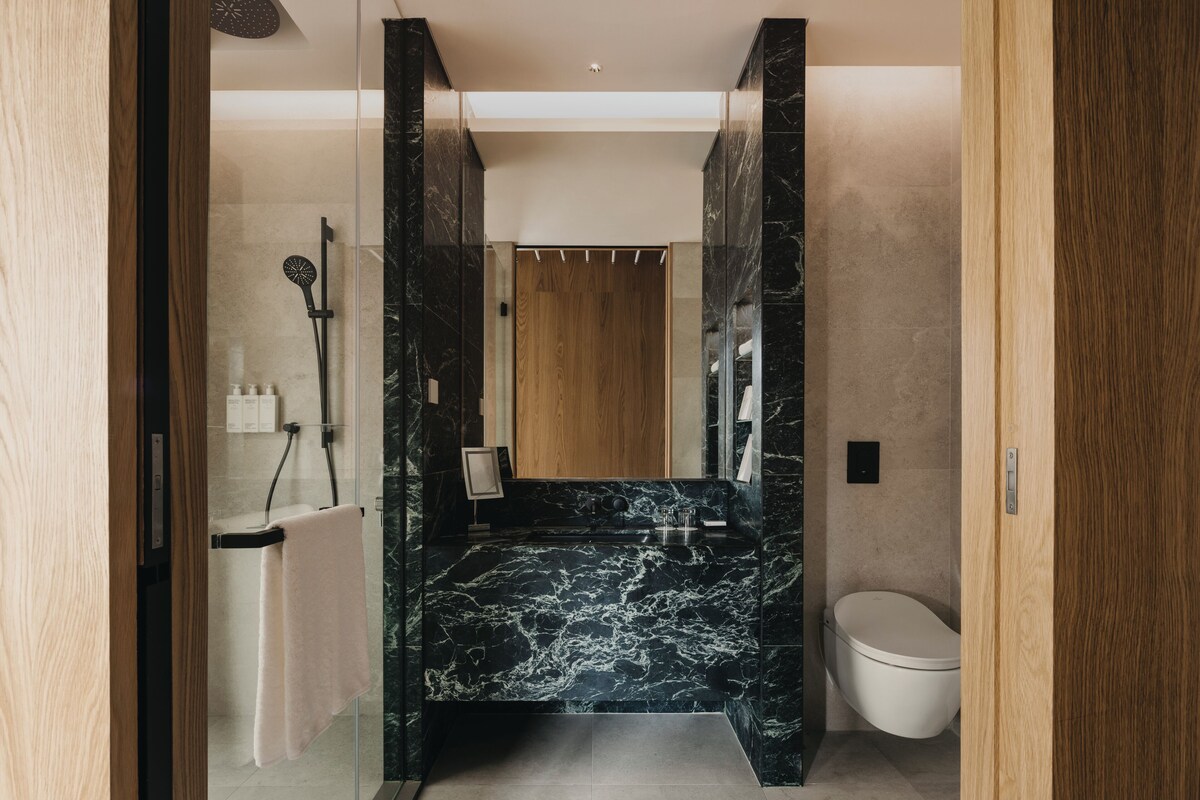 A modern bathroom with a marble vanity, a glass shower enclosure, and a wooden door.