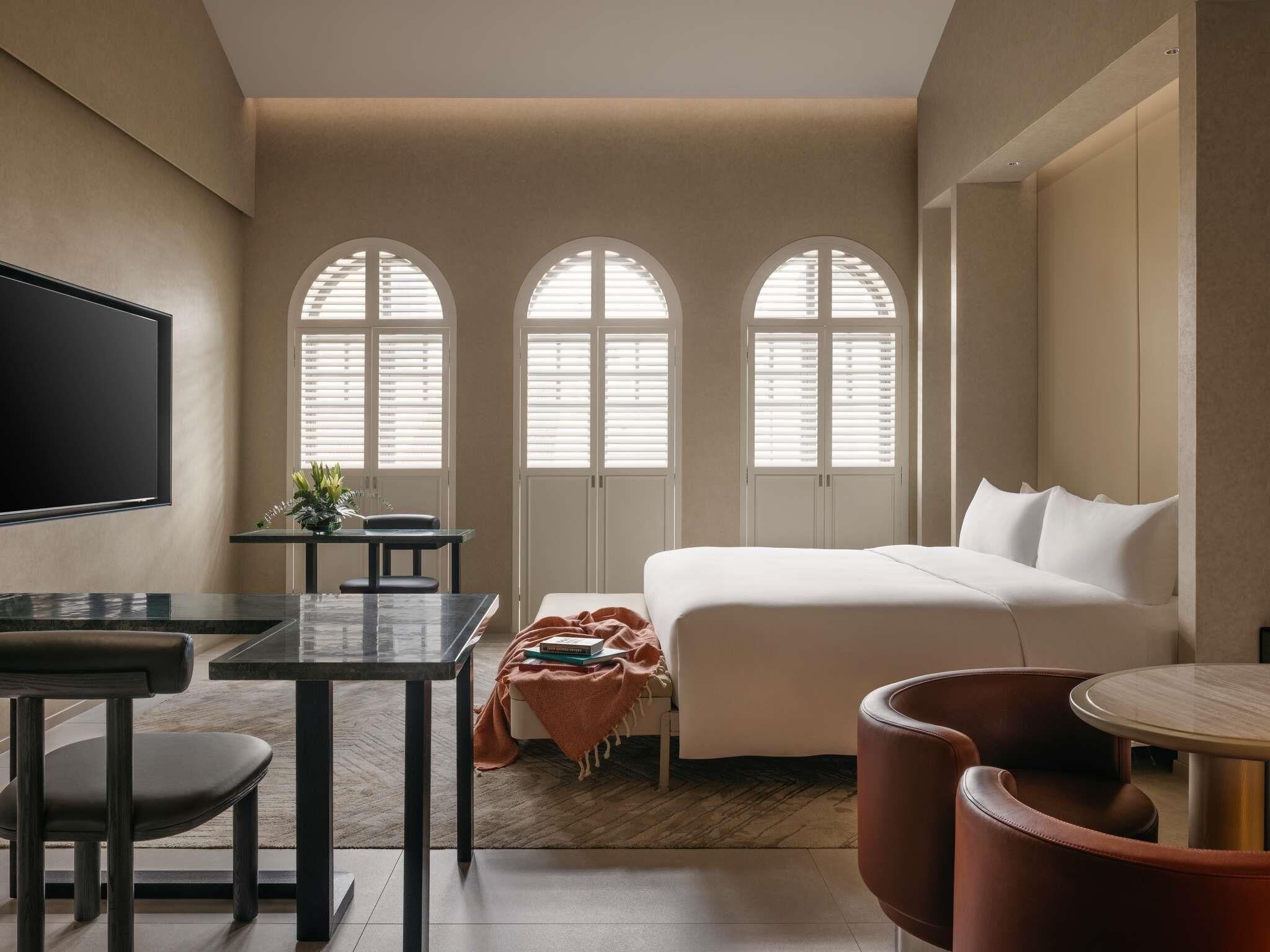 Een moderne hotelkamer met een bed, een bureau, een stoel, een televisie en gebogen ramen.