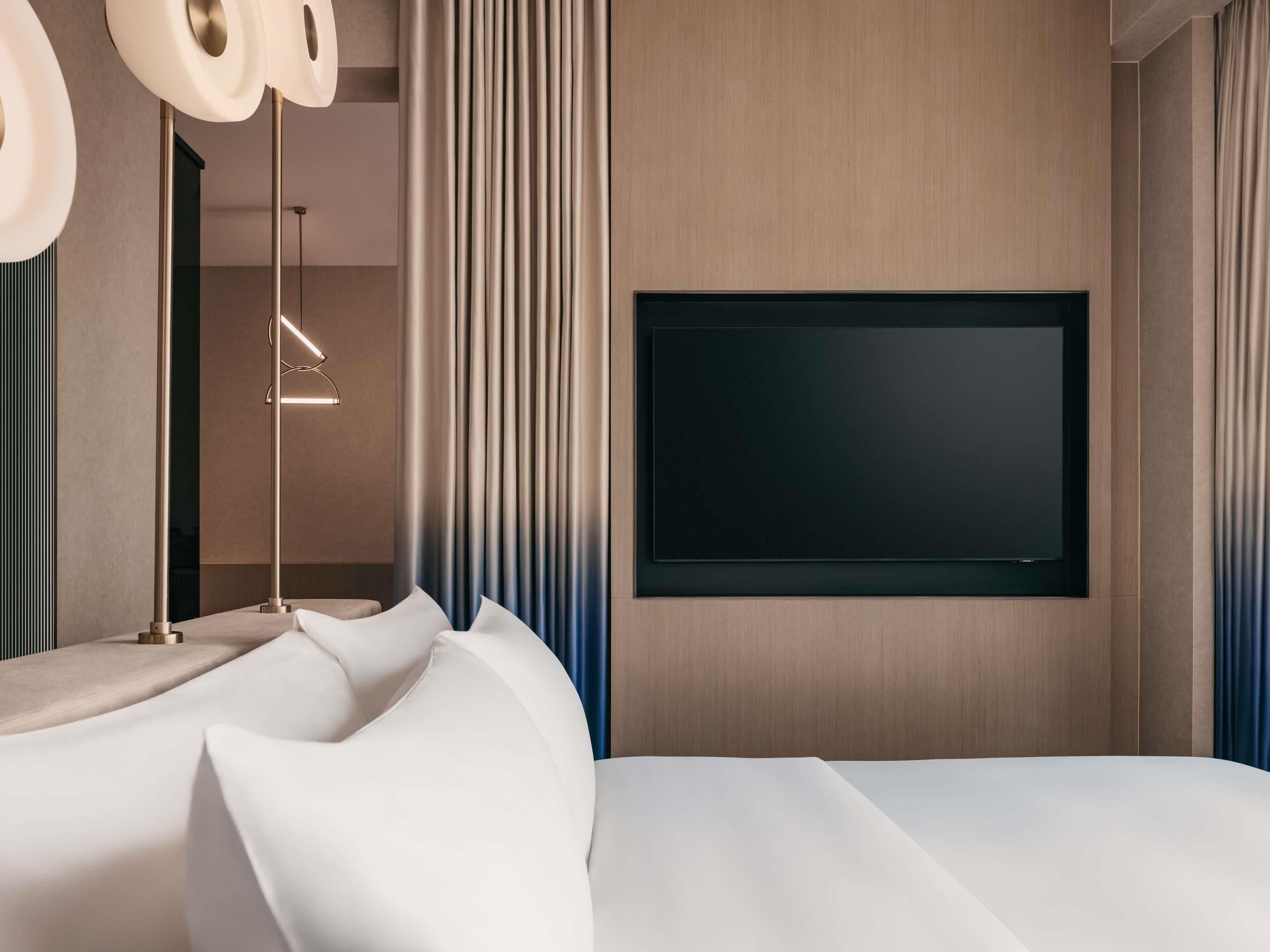 Un dormitorio moderno con una cama grande, un televisor de pantalla plana en la pared y una mesita de noche con lámpara.