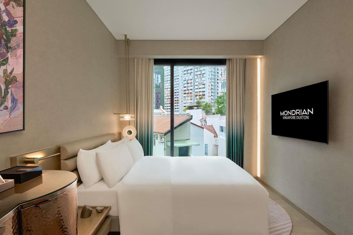 Een moderne hotelkamer met een bed, nachtkastje, lamp en een televisie waarop de naam van het hotel staat.