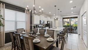A modern kitchen with white cabinets, a stainless steel refrigerator, and a dining area with a dark wooden table and chairs. - Solterra Resort 5 bedroom Private Pool/Spa Home (Davenport)
