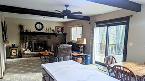 A spacious living area with a fireplace, a dining table, and a large window offering a view of the outdoors. - Secluded Chalet in Michaywe w/ pool access. Golf + Ski/Snowmobile paradise. (Gaylord)