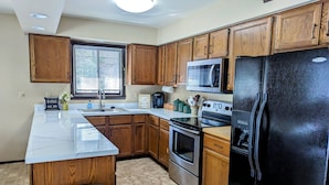 A modern kitchen with wooden cabinets, a black refrigerator, a microwave, an oven, and a sink. - Secluded Chalet in Michaywe w/ pool access. Golf + Ski/Snowmobile paradise. (Gaylord)