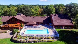 A lodge with a swimming pool, outdoor seating, and a forested backdrop. - Secluded Chalet in Michaywe w/ pool access. Golf + Ski/Snowmobile paradise. (Gaylord)